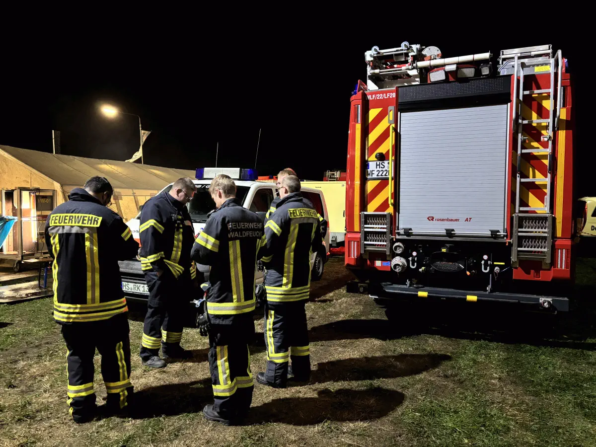 Feuerwehrleute besprechen sich vor einem Feuerwehrauto.