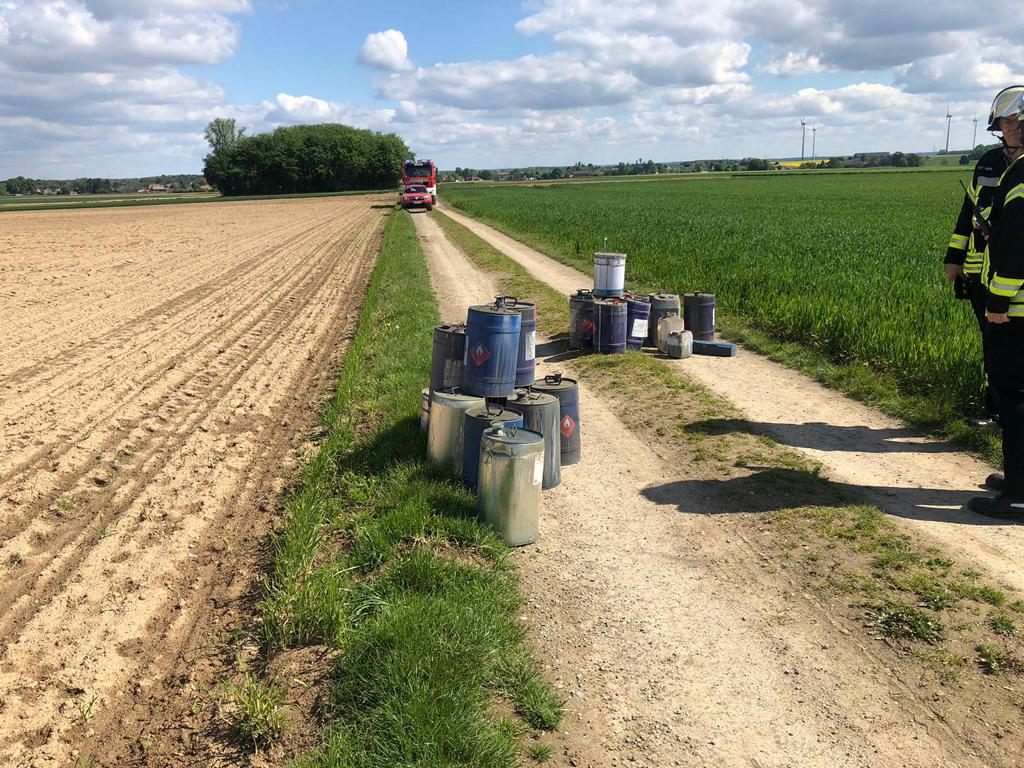 Ölfässer auf einem Feldweg. Feuerwehrautos im Hintergrund.
