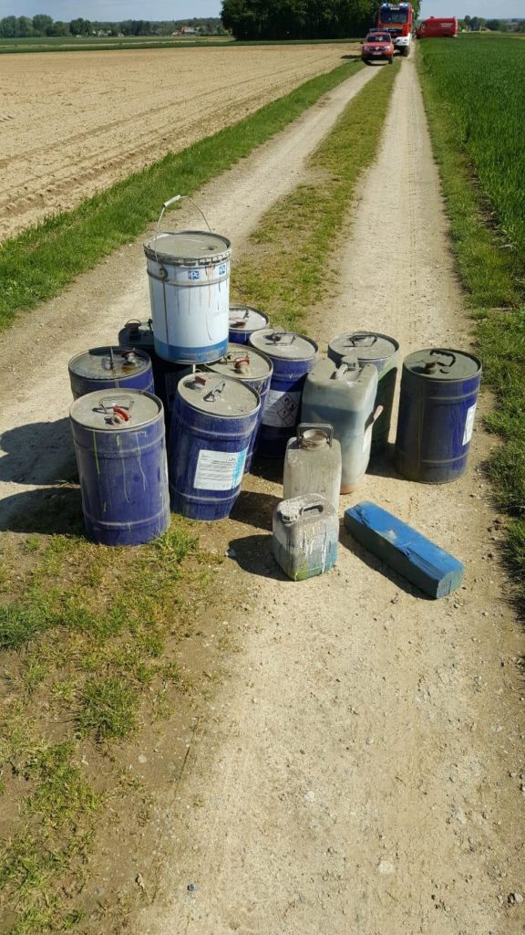 Ölfässer auf einem Feldweg. Nähere Aufnahme. Feuerwehrautos im Hintergrund.
