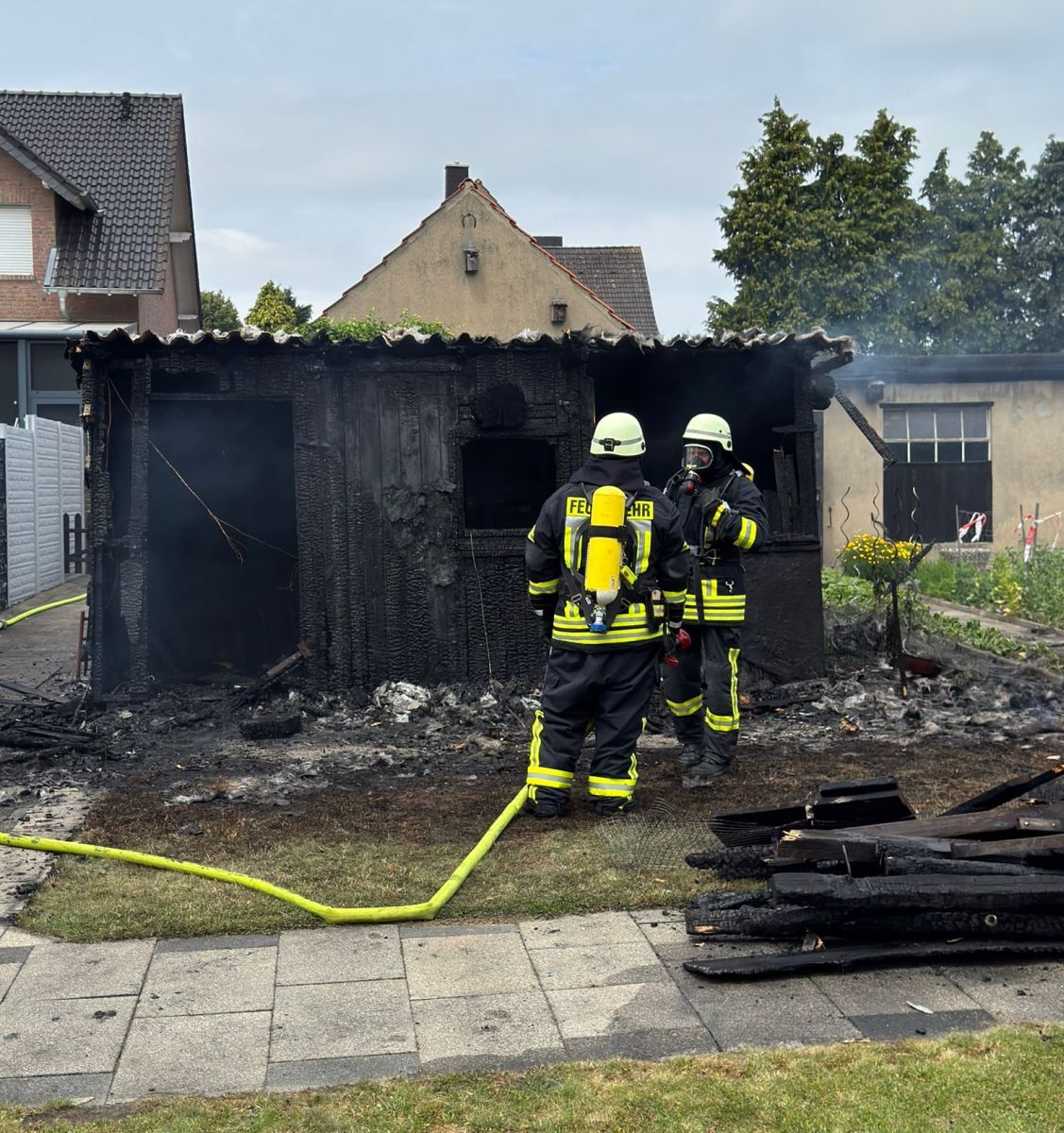 zwei Feuerwehrleute vor abgebrannter Gartenlaube