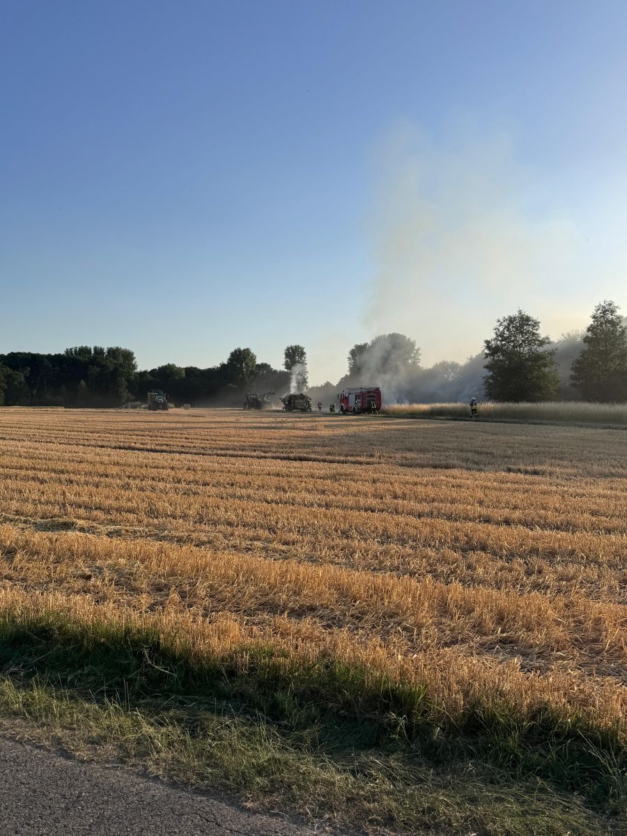 qualmende Landwirtschaftsmaschine mit Feuerwehrleuten und Feuerwehrauto - Bild aus der Ferne