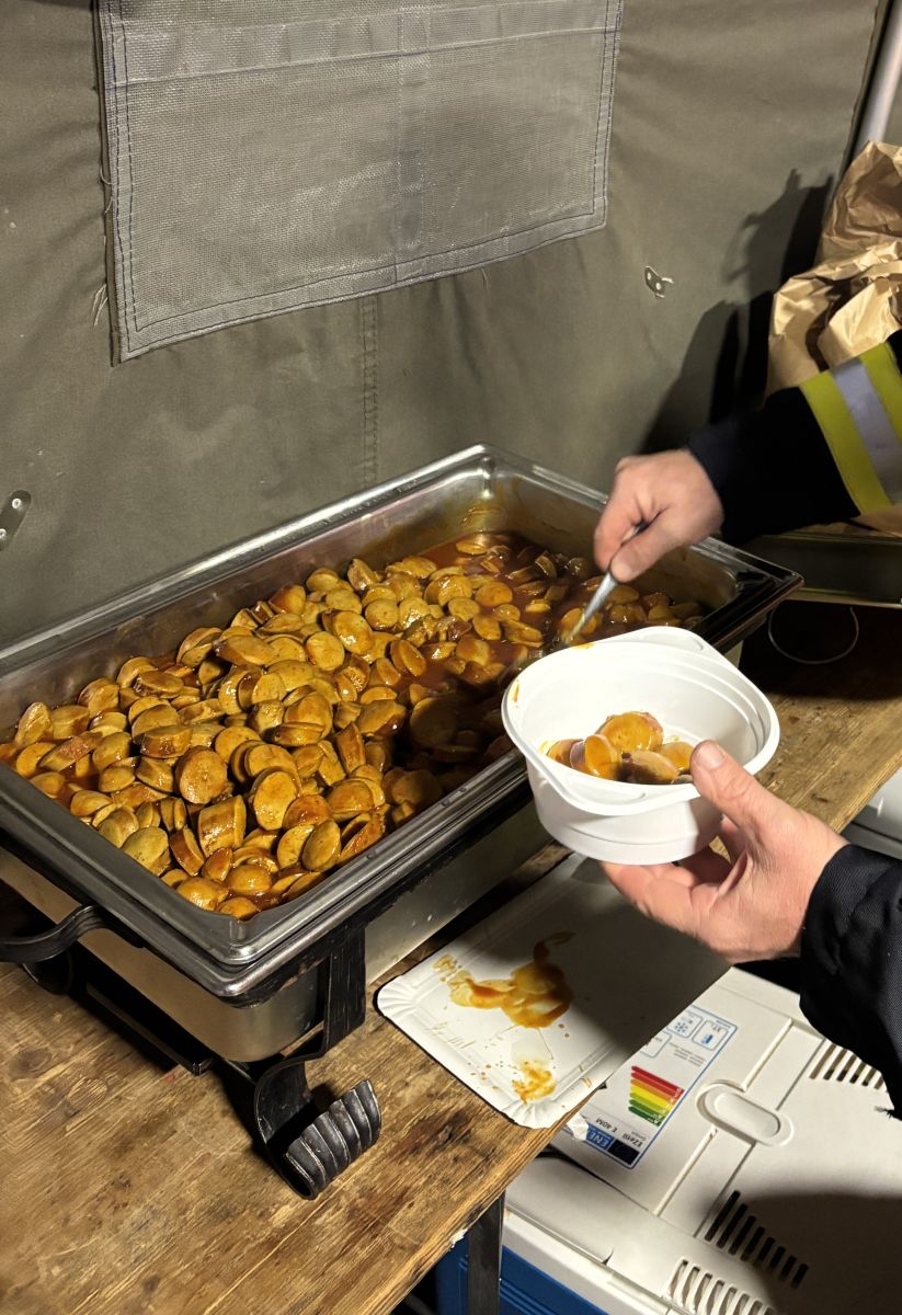 Feuerwehrmann löffelt Currywurst in einen Becher.