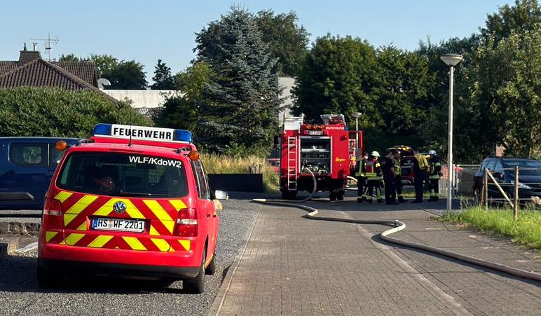 Einsatzleitwagen mit Feuerwehrfahrzeug und Feuerwehrleuten im Hintergrund. Die Wasserversorgung verläuft ebenfalls durch das Bild.