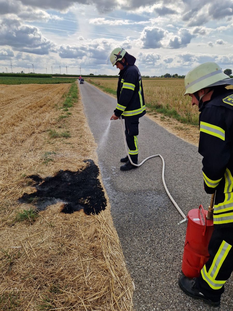 2 Feuerwehrleute, welche mit einer Kübelsprinte einen Schwelbrand im Stoppelfeld löschen