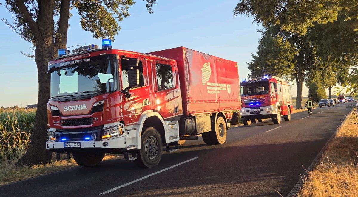 Zwei Feuerwehrautos am Straßenrand mit Blaulicht. Ein Feuerwehrmann im Hintergrund.